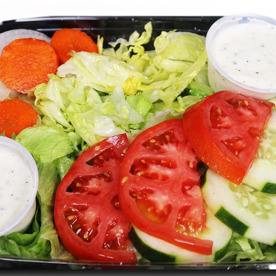Fresh garden salad with lettuce, tomatoes, cucumbers, carrots, onions, and two cups of creamy dressing in a black tray.
