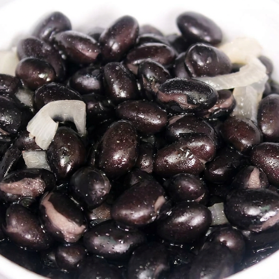 Close-up of glossy black beans mixed with sliced onions in a white bowl.