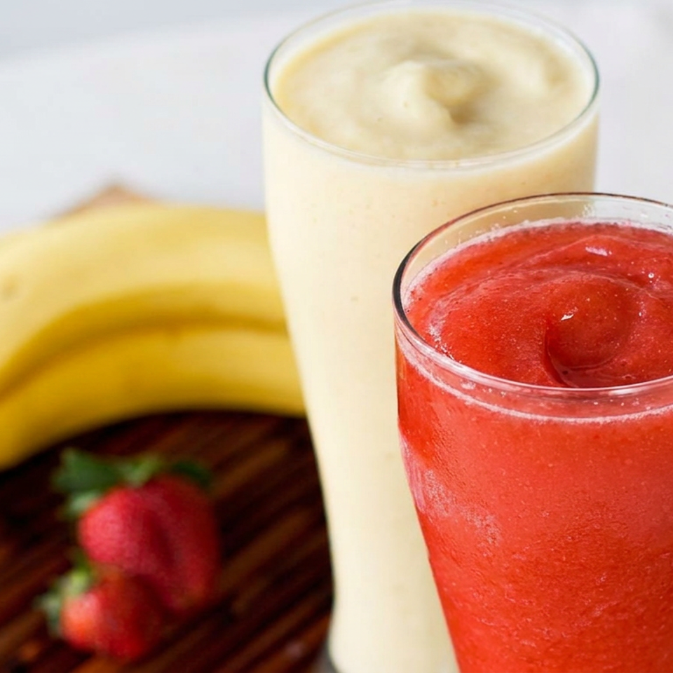Red strawberry smoothie and creamy banana smoothie served with fresh bananas and strawberries on a wooden board.